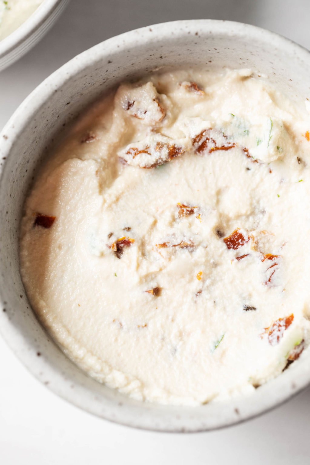 A bowl of vegan tofu cream cheese, which has been mixed up with chopped sun-dried tomatoes.