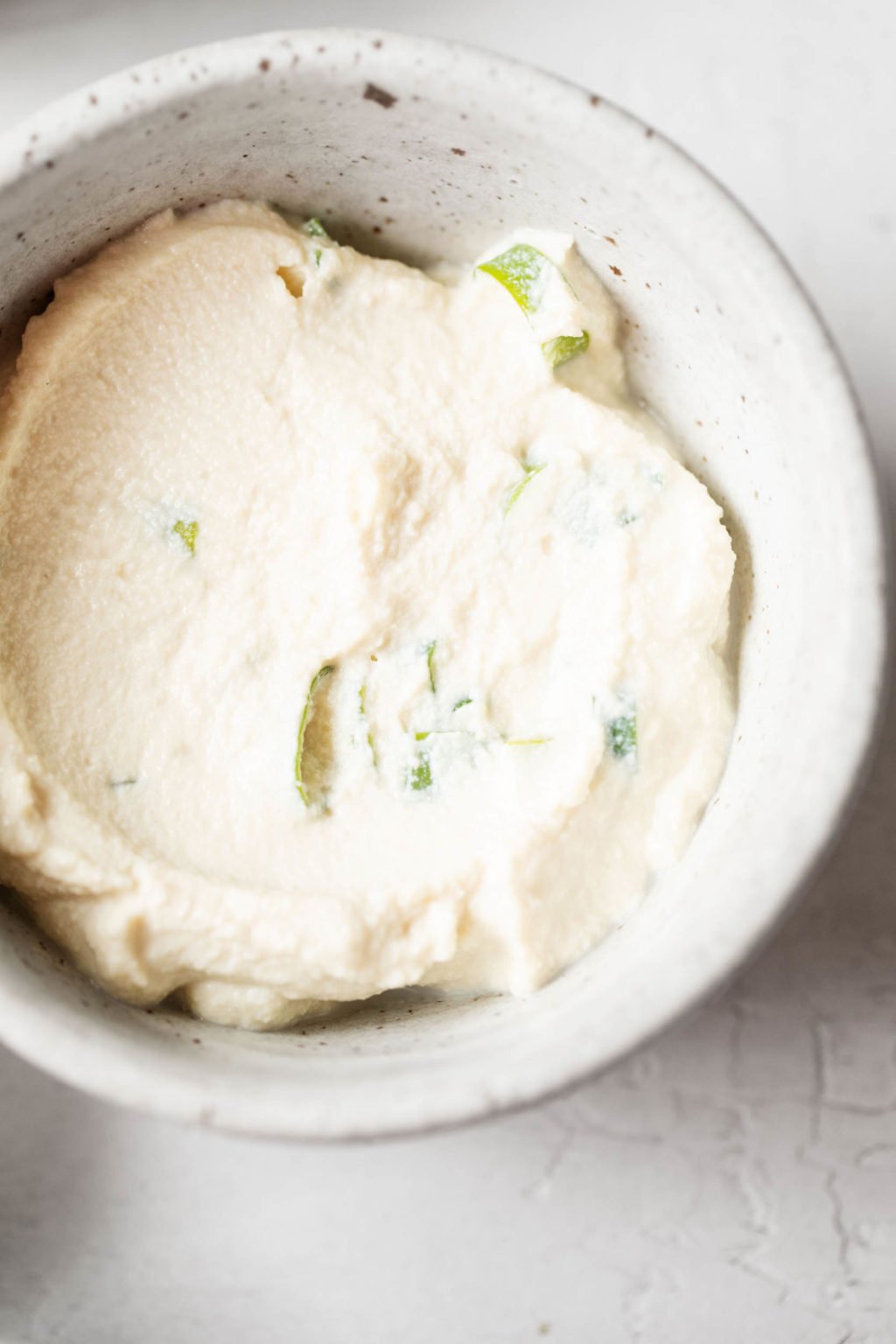 A creamy vegan spread, pictured top down in a small bowl, with scallions mixed in.