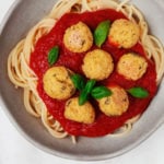 Homemade vegan protein is served over spaghetti and red sauce, in a ceramic bowl. It rests on a white surface.