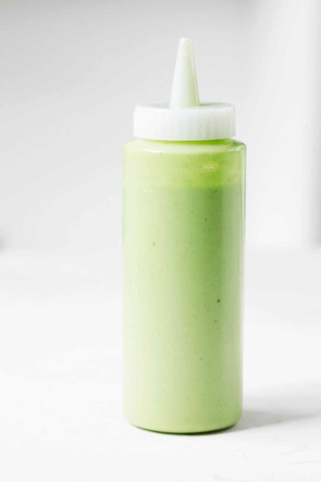 A plastic squeeze bottle holds a pale green sauce. It is pictured against a white background.
