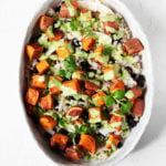 A large, oval serving dish is filled with coconut sweet potato rice and beans, and it's covered with a green sauce.