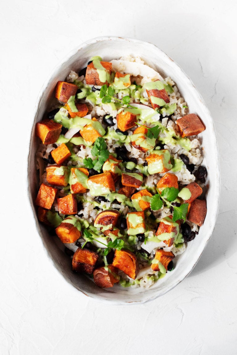A large, oval serving dish is filled with coconut sweet potato rice and beans, and it's covered with a green sauce.