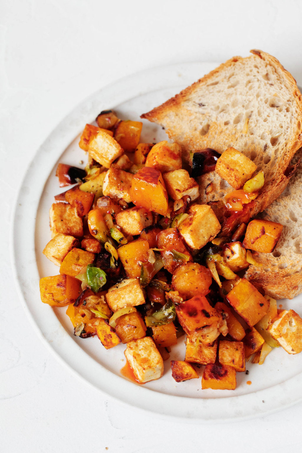 A round, white plate serves a slice of bread and an orange-colored butternut squash hash.