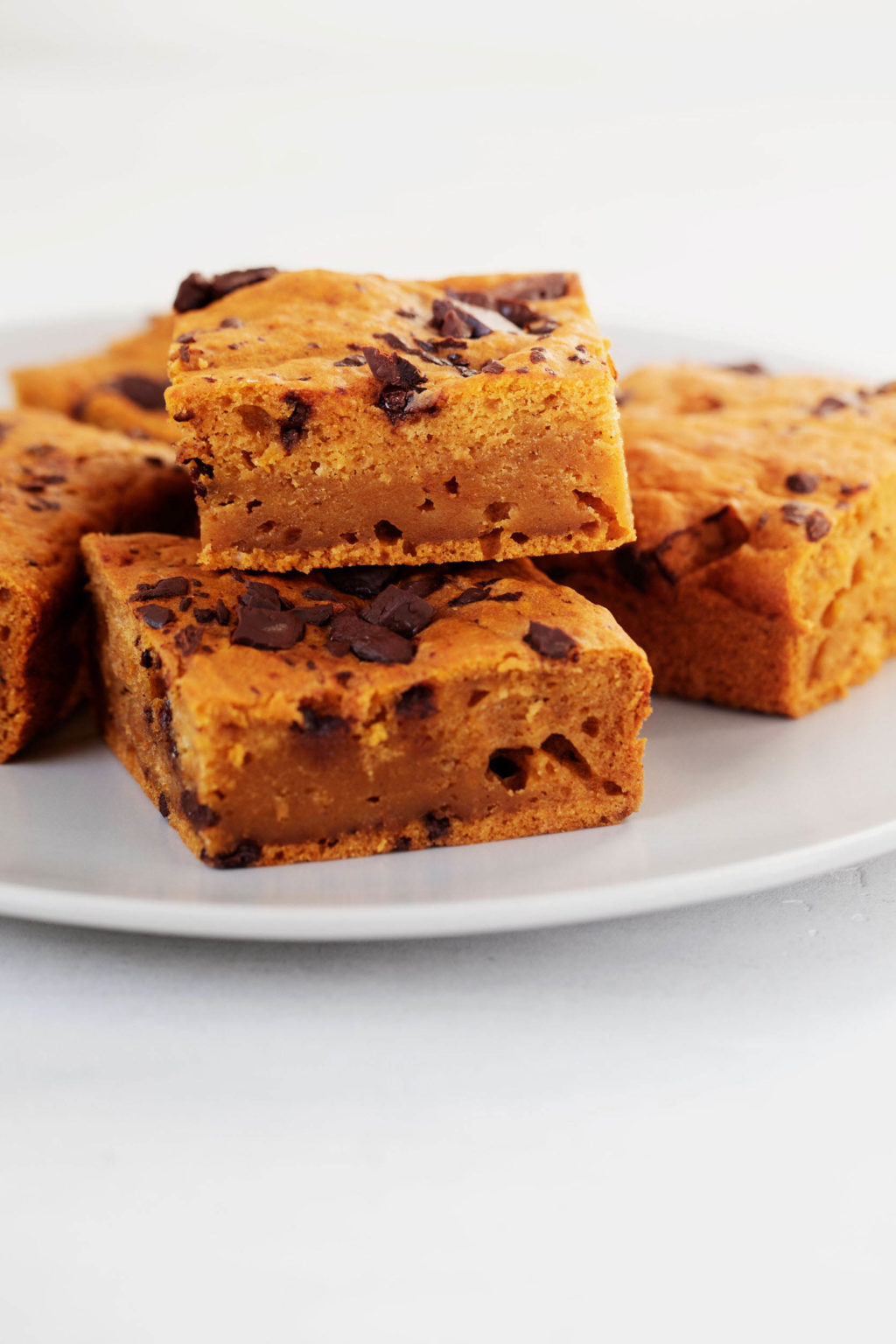 A stack of vegan blondies, which have been made with the addition of pumpkin and chocolate, rest on a white surface.