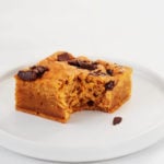 A cakey vegan pumpkin chocolate chip blondie is resting on a small, rimmed, white dessert plate.