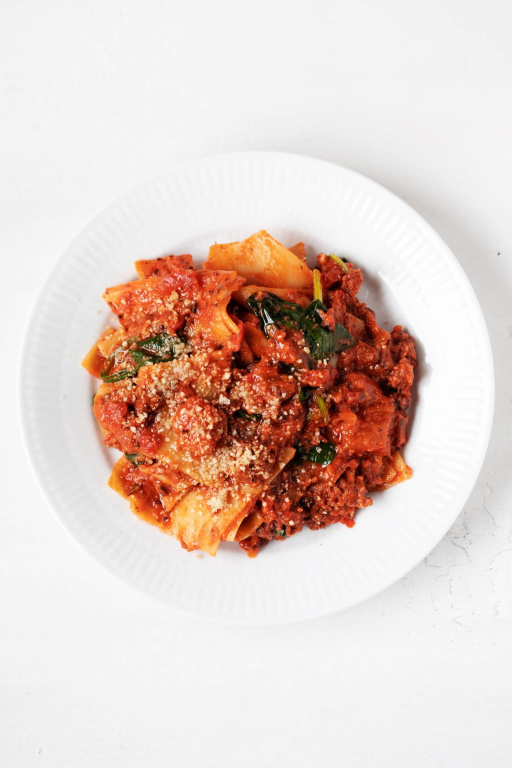 A round white serving plate holds a generous helping of creamy vegan skillet lasagna. It rests on a white surface.