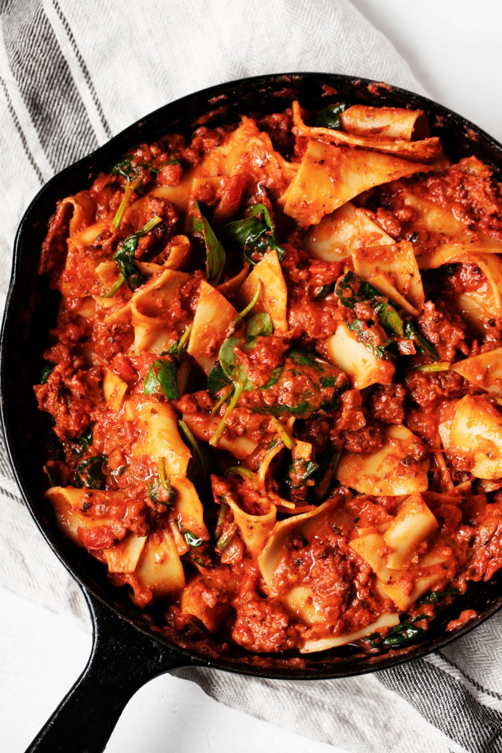 A large, cast iron skillet has been filled with a creamy vegan skillet lasagna and baby spinach.