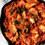 A large, cast iron skillet has been filled with a creamy vegan skillet lasagna and baby spinach.