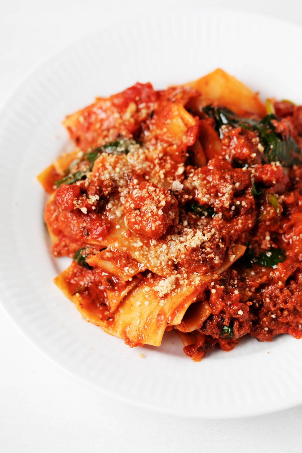 A white, shallow bowl has been piled high with a plant-based pasta dish, covered in red tomato sauce.