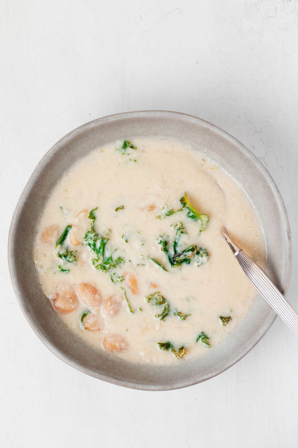 An overhead image of a cream soup, which is flecked with green pieces of kale.