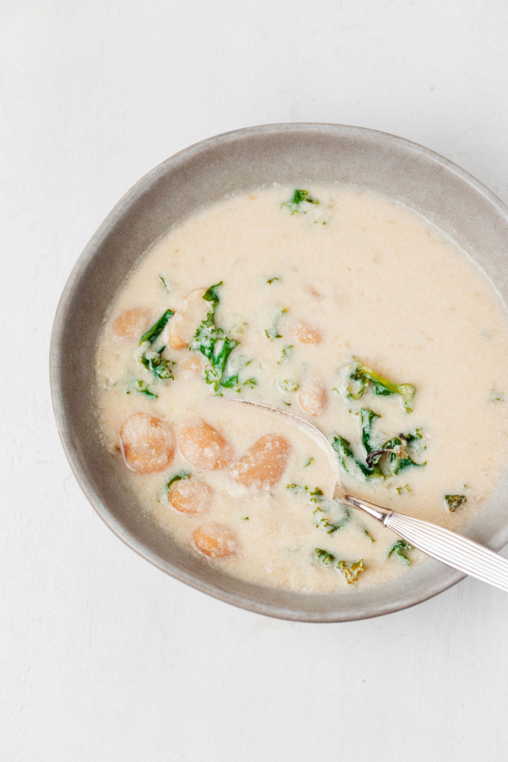 A gray, ceramic bowl holds a creamy white bean soup. A spoon is resting in it.