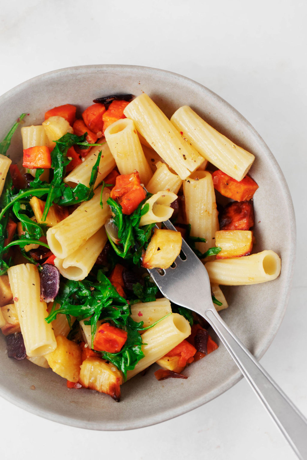 An overhead image of rigatoni, which have been mixed with arugula and roasted root vegetables.