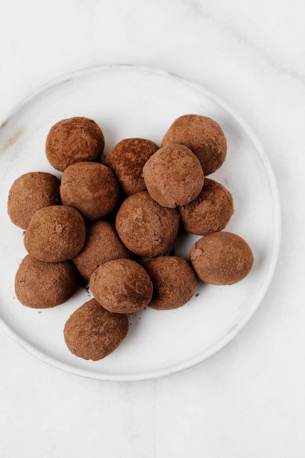 Round, cocoa-dusted espresso truffles are resting on a small, white plate.