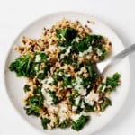 A round, white plate is covered with cumin-spiced lentils & rice, a serving fork, and a drizzle of pale-colored tahini sauce.