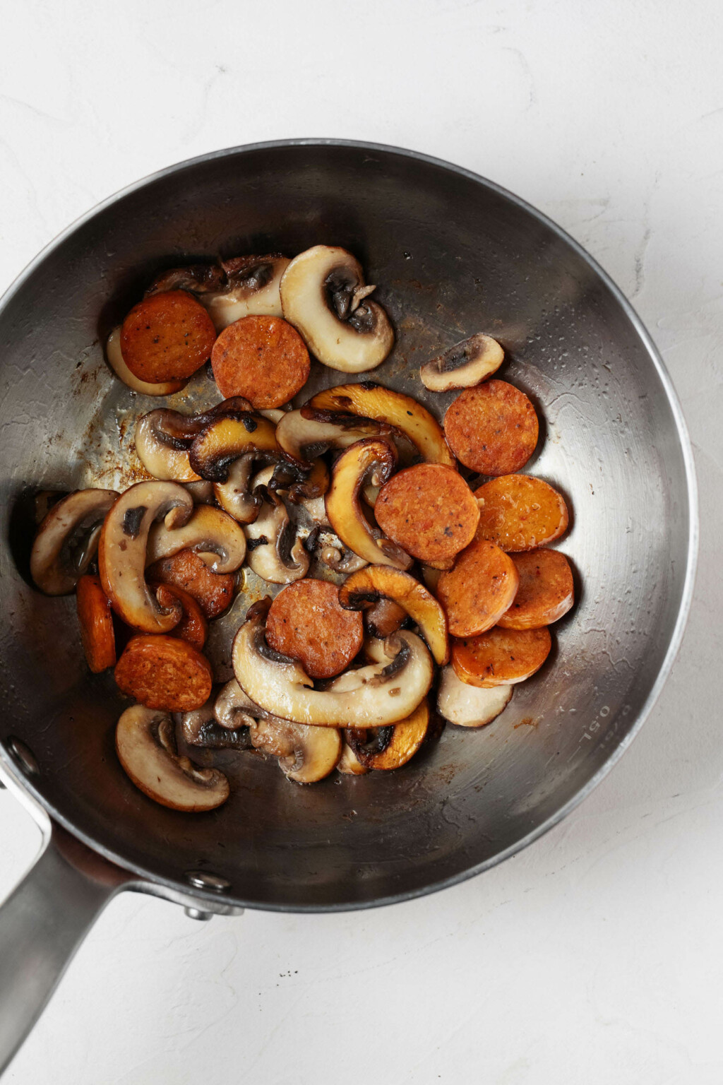 A silver skillet is being used to sauté sliced mushrooms and sausage.