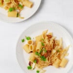 Two plates of caramelized cabbage onion pasta are resting on a white surface. Each has been lightly garnished with chopped parsley.