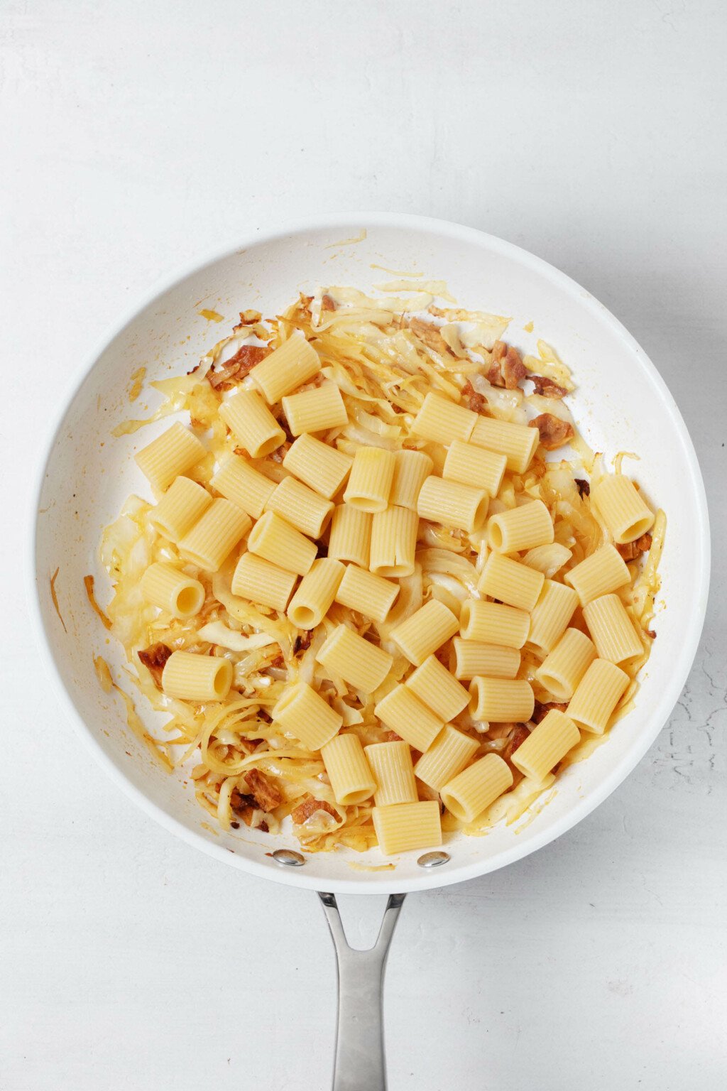 Cooked pasta has just been added to a skillet with sautéed vegetables.