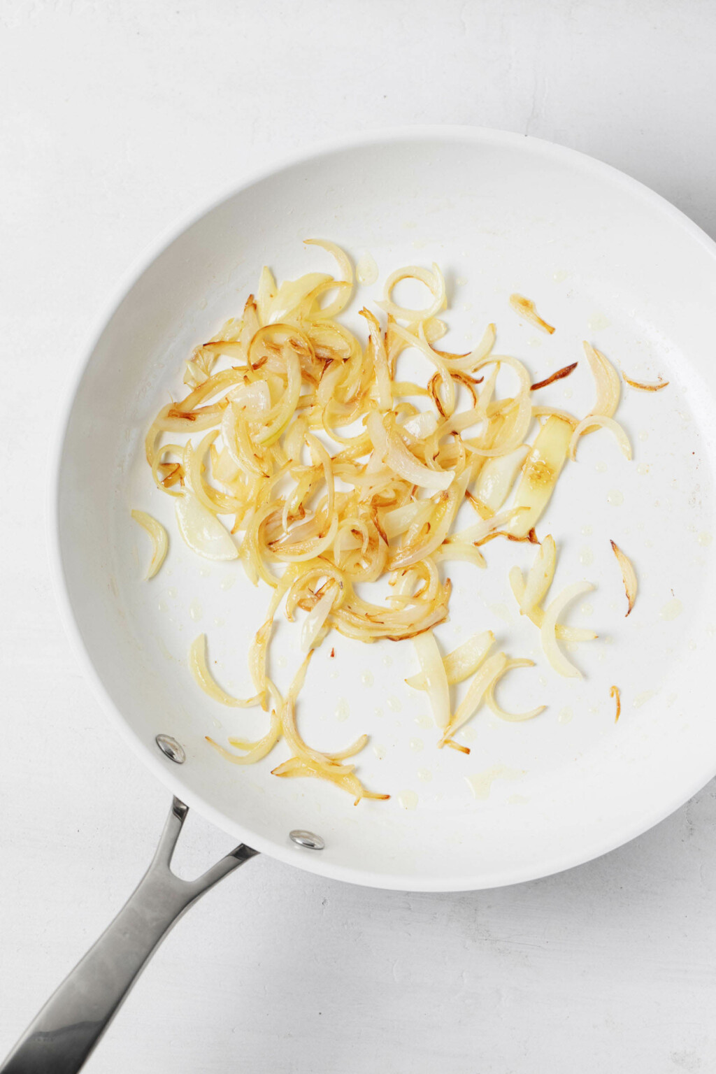A white frying pan contains lightly browned onions.