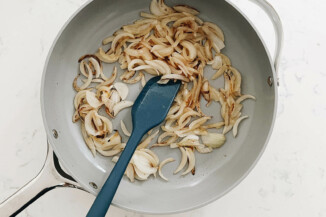 A gray frying pan contains lightly browned onions.