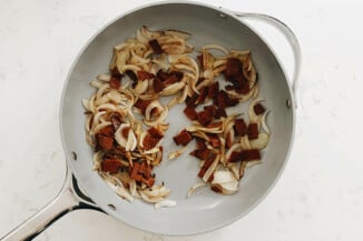 A white frying pan holds vegan bacon and caramelized onions.