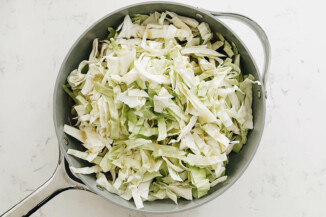 A large gray sauté pan has just been filled with sliced cabbage.