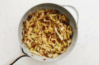 Cabbage, onions, and vegan bacon have been cooked down in a large, gray sauté pan.