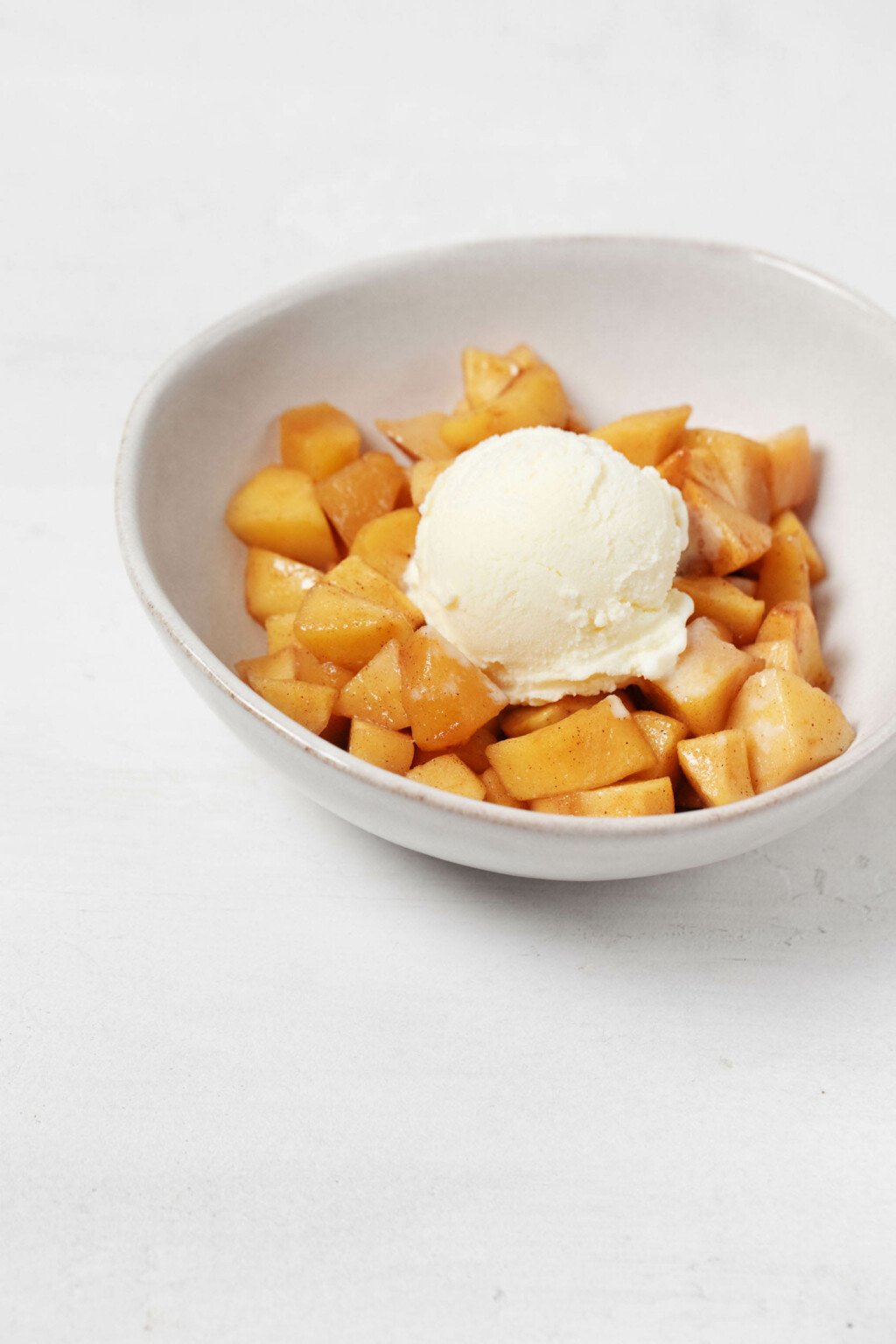 An angled image of a bowl of baked apples, topped with a round scoop of vanilla ice cream.