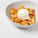 An angled image of a bowl of baked apples, topped with a round scoop of vanilla ice cream.