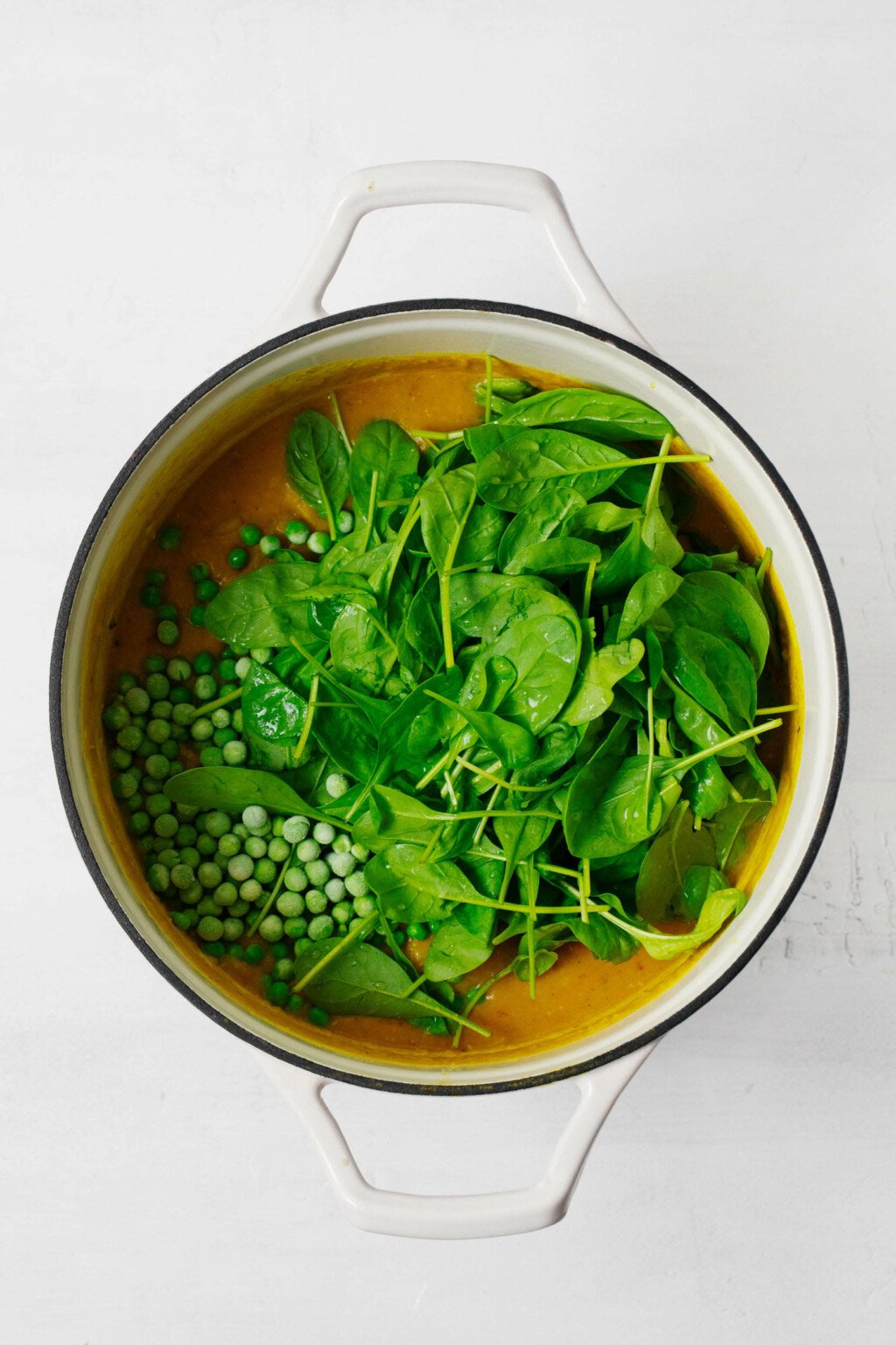 A large, white pot is filled with spinach, peas, and broth.