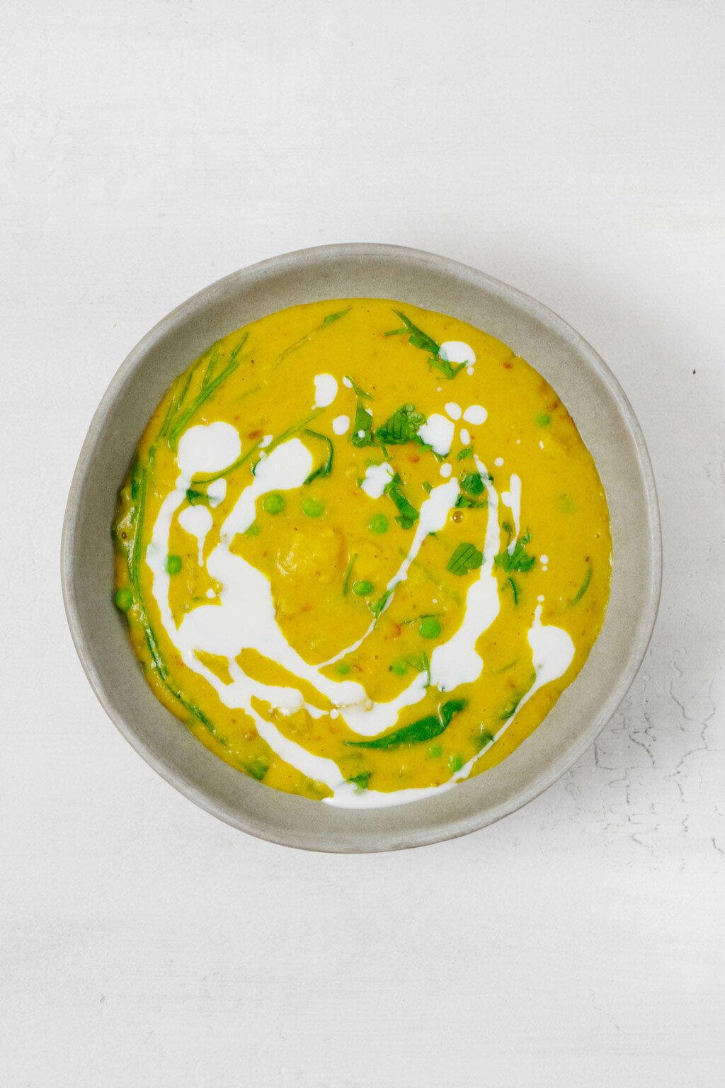 An overhead image of a gray, ceramic bowl that's filled with a golden colored, plant-based soup.