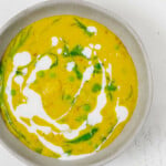 An overhead image of a pot of curried potatoes, lentils, and peas, topped with cashew cream,