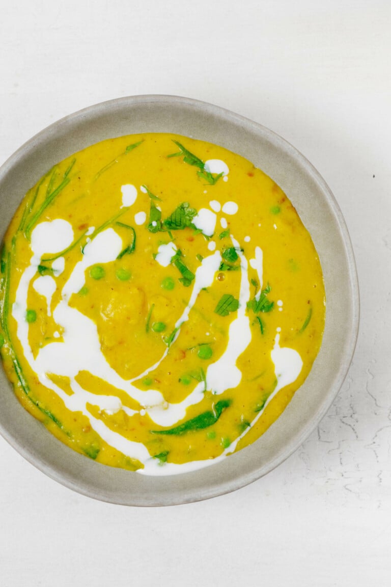 An overhead image of a pot of curried potatoes, lentils, and peas, topped with cashew cream,