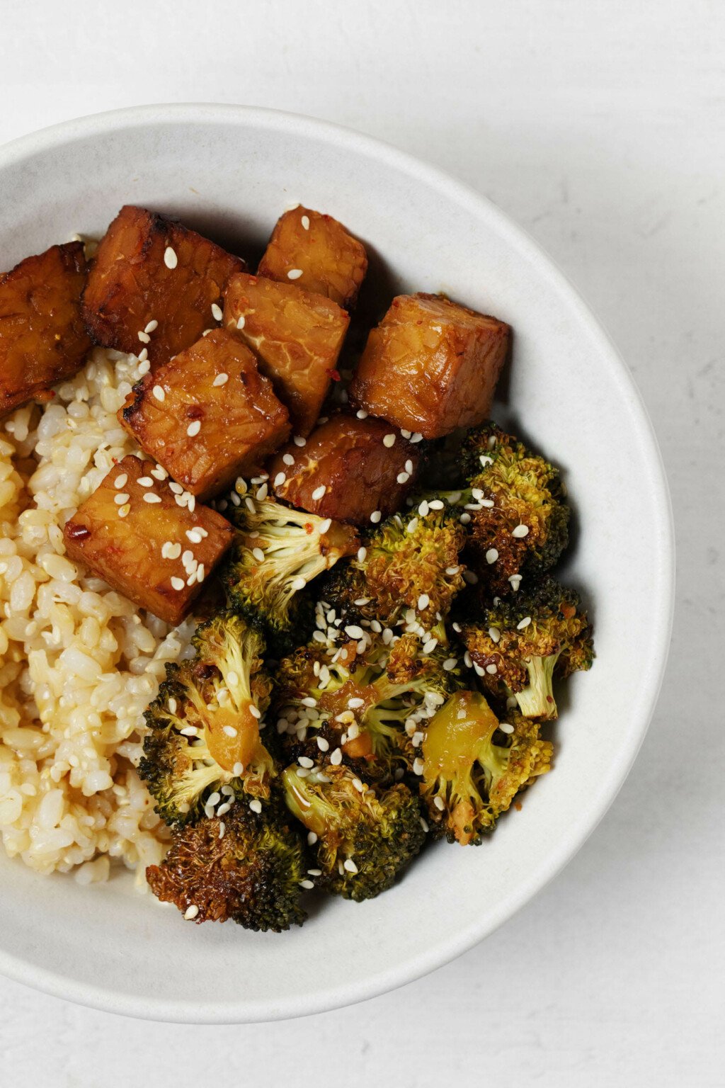 A closeup image of a vegan protein with glazed tempeh, sesame seeds, and brown rice.