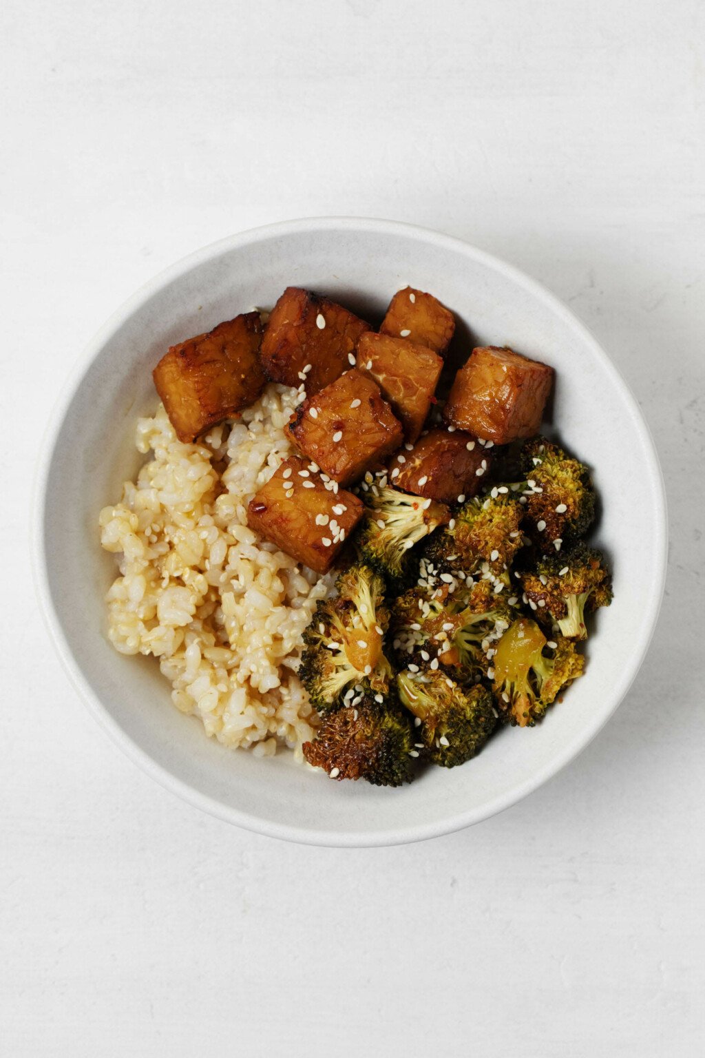 Sheet pan tempeh & broccoli are resting in a bowl with cooked rice.