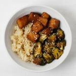 Sheet pan tempeh & broccoli are resting in a bowl with cooked rice.
