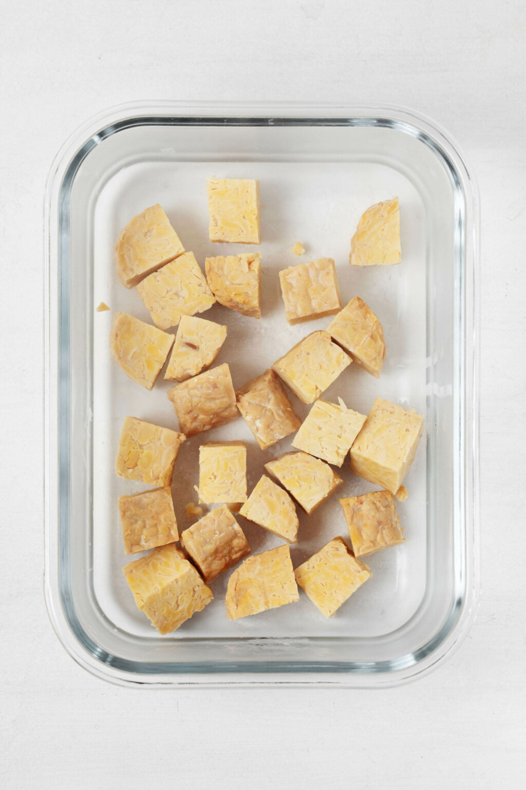 Cubed tempeh is resting in a clear, rectangular storage dish.