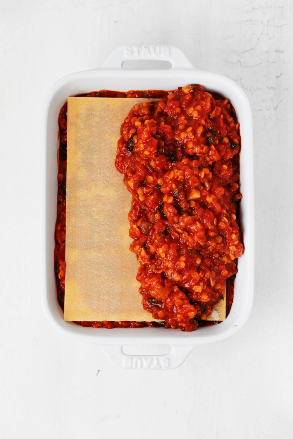 A pasta dish is being assembled in a white, rectangular baker.