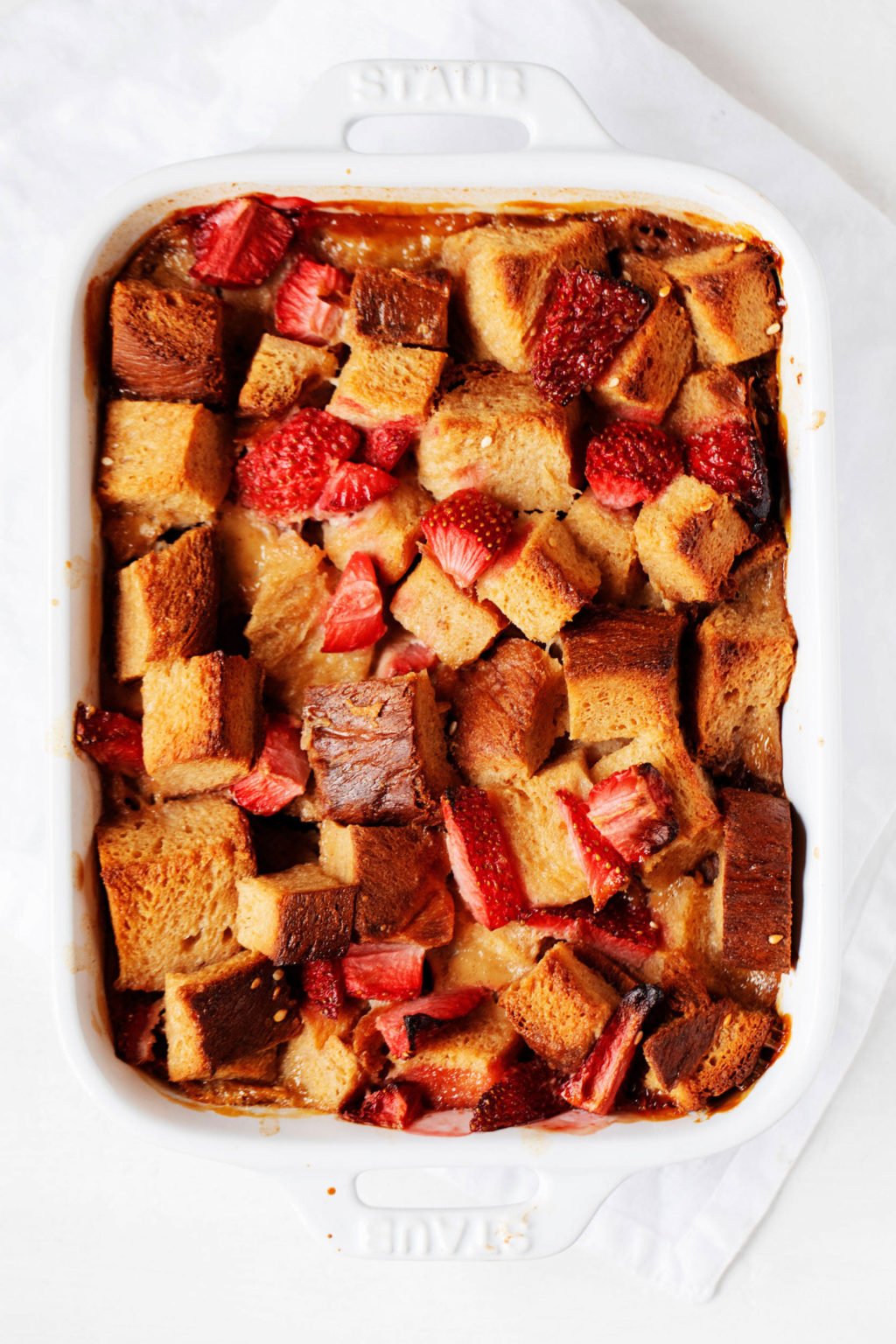 A rectangular, white baker holds a dish of baked French toast and strawberries.