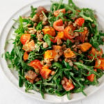 A round white plate has been covered in a colorful, creamy lentil tahini sweet potato salad.