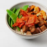 A chili roasted cauliflower and brown rice kimchi bowl is resting on a white surface.