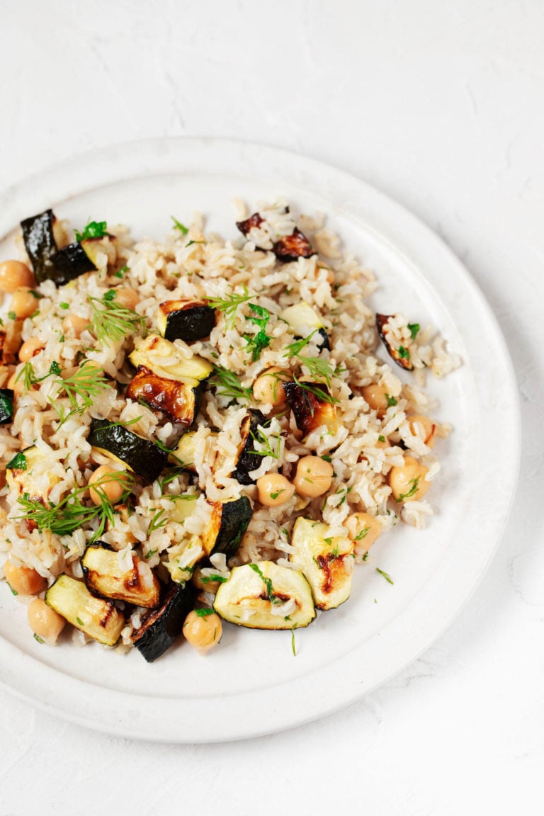 An overhead image of a plate covered in zucchini chickpea rice, which is garnished with fresh dill.