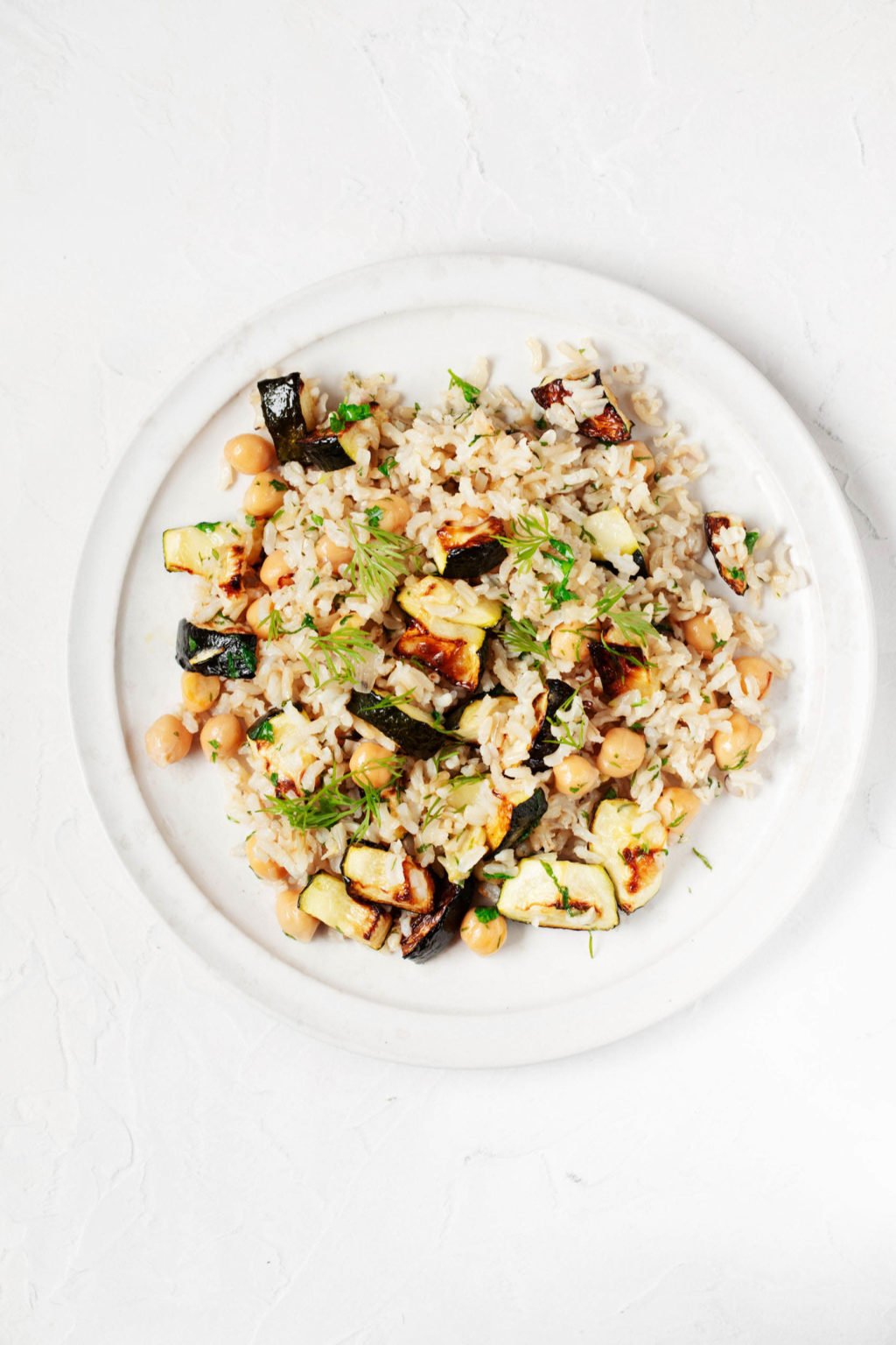 A white, round plate serves a zucchini, rice, and chickpea dish. It rests on a white surface.