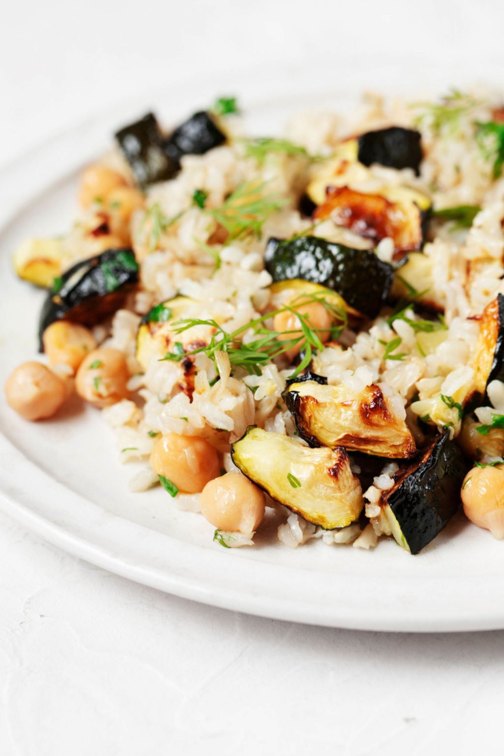 A white, rimmed plate is covered with a dish of whole grains, vegetables, and beans. It's garnished with herbs and rests on a white surface. 