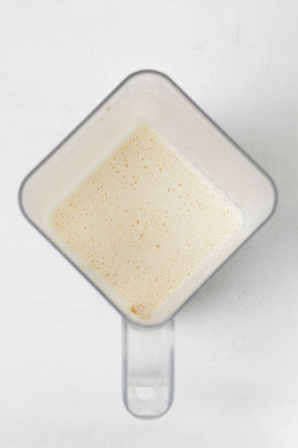 Non-dairy milk is pictured from overhead in the square container of a standing blender.