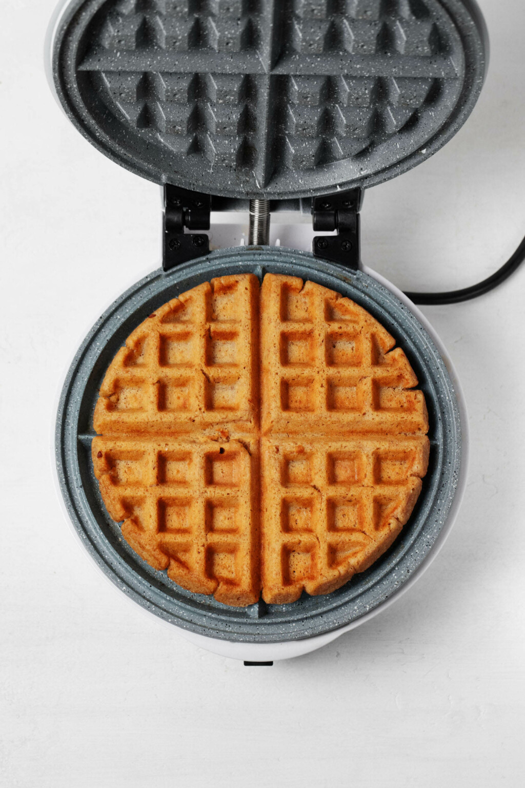 An overhead image of a Belgian waffle maker, which is being used to make a light and crispy vegan peanut butter waffle.