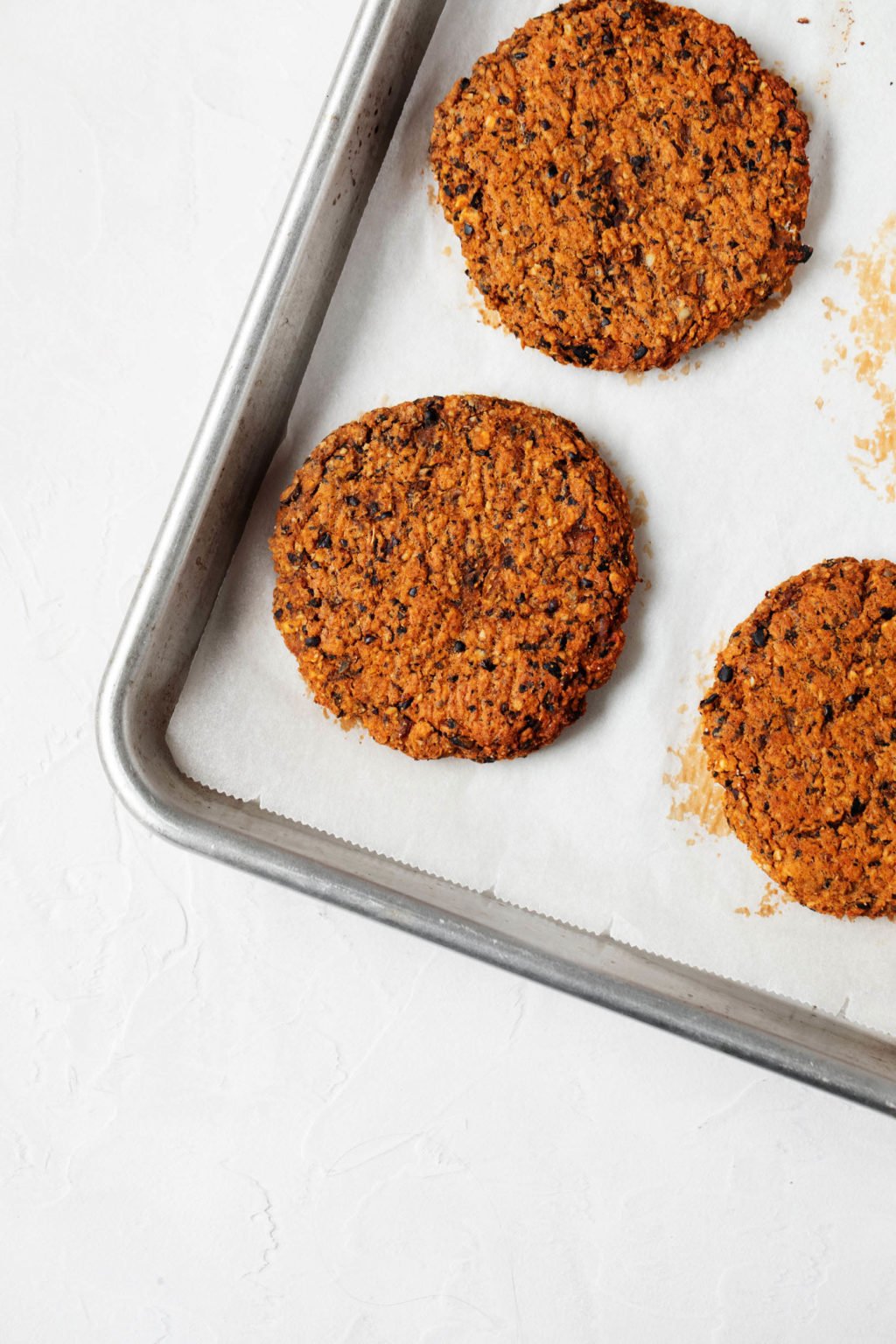 Black bean sweet potato burgers are arranged on a parchment lined baking sheet. 