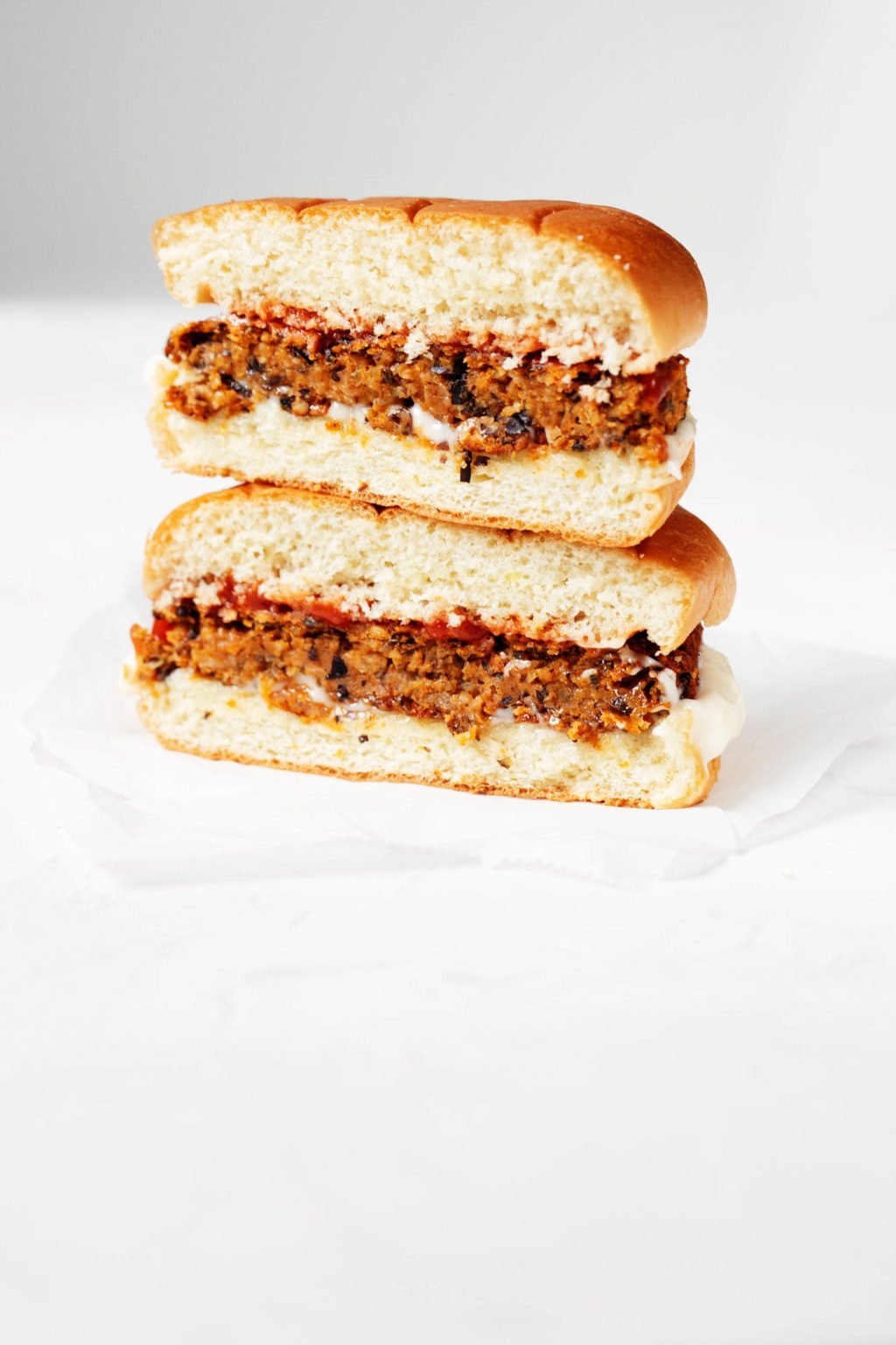 Vegan black bean sweet potatoes are served on a hamburger bun with ketchup and mayonnaise. The burger is cut in half, revealing a crosswise section.