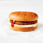 A plant-based burger is piled onto a simple burger bun with mayonnaise and ketchup. It's resting on a small piece of parchment paper.