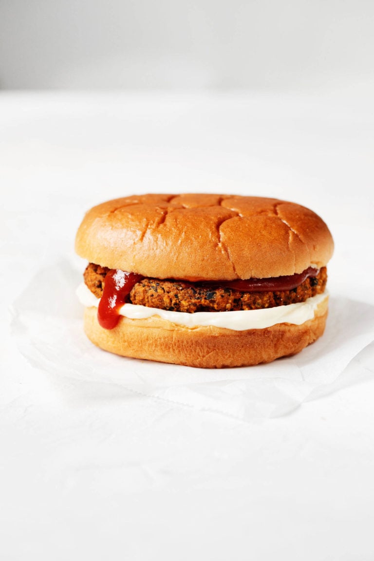 A plant-based burger is piled onto a simple burger bun with mayonnaise and ketchup. It's resting on a small piece of parchment paper.