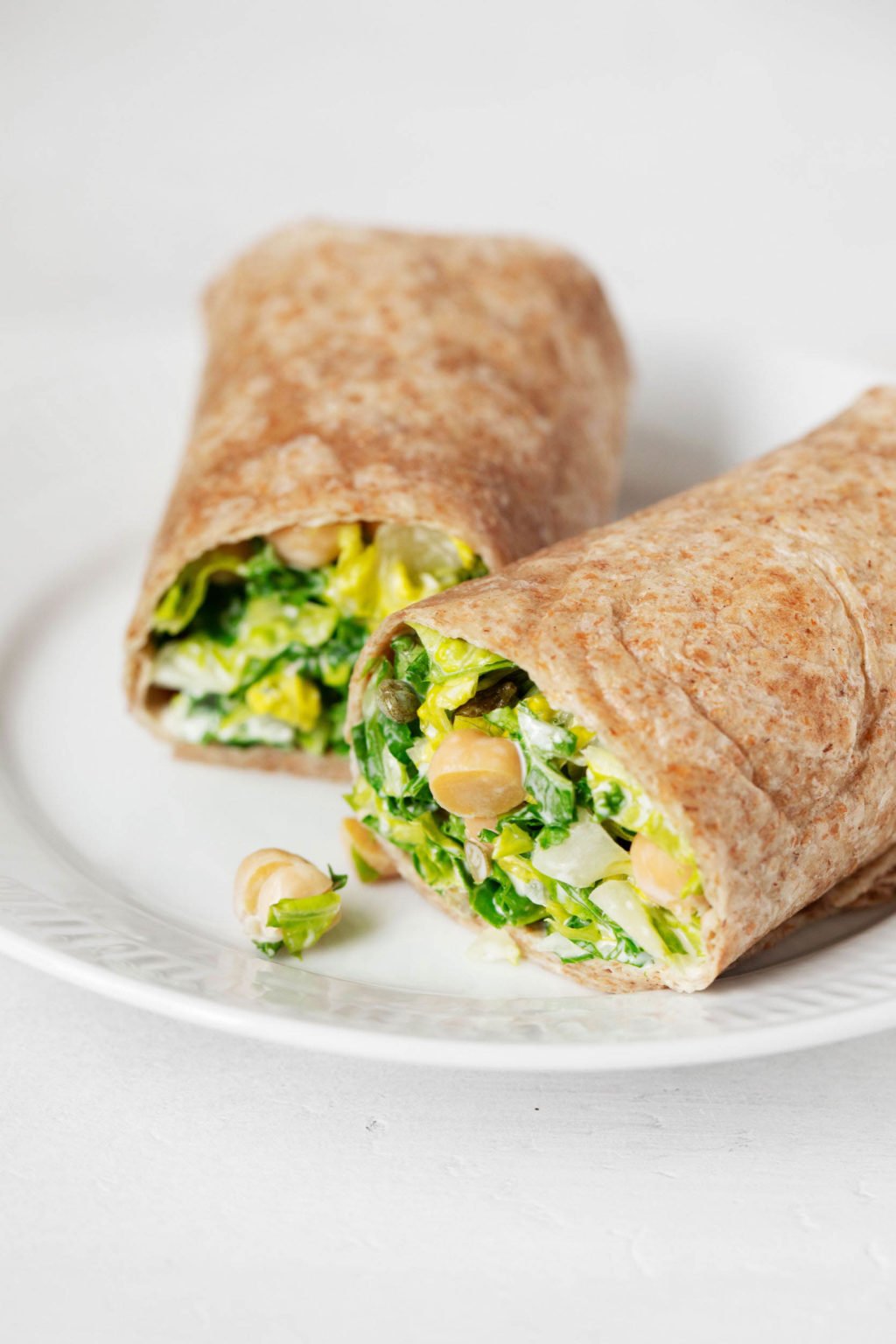 A close up of a whole wheat burrito, which has been stuffed with leafy greens and beans, then cut and served on a white, rimmed plate.
